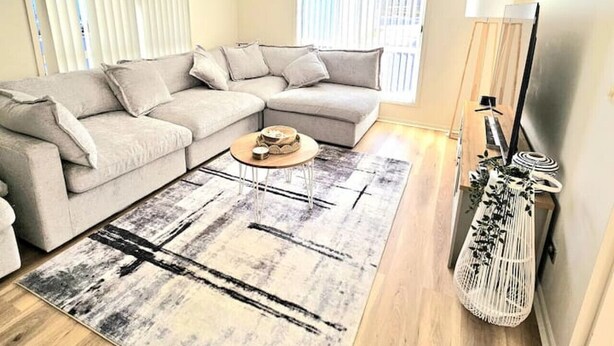 A living room with a sectional sofa, a coffee table, a patterned rug, a ceiling fan, and a TV stand with a lamp. - Cosy Villa - Pool Tennis & More | Pay 2 Stay 3 (Saint Georges Basin)