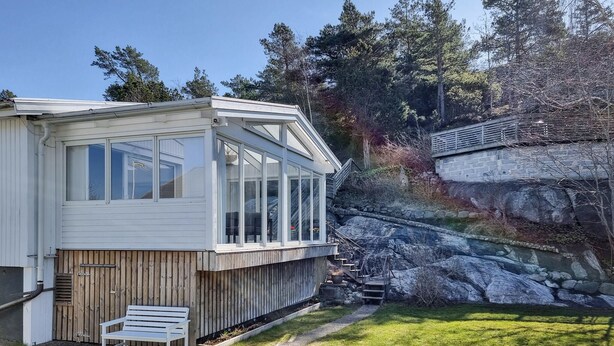 Une maison moderne dotée d’une grande baie vitrée, d’une terrasse en bois et d’un mur de soutènement en pierre.