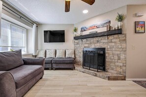 A living room with a fireplace, a sofa, a flat-screen TV, and a stone wall. - Afton Oaks: Cozy Westside Retreat • 2BR Townhome Near Garden of the Gods (Colorado Springs)