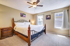 A bedroom with a bed, a nightstand, a ceiling fan, a window with curtains, and a wall-mounted picture. - Afton Oaks: Cozy Westside Retreat • 2BR Townhome Near Garden of the Gods (Colorado Springs)