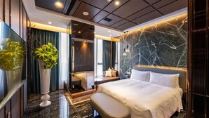 A modern hotel room with a large bed, a seating area, a mirror, and a large plant.