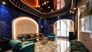 A modern lounge with a curved ceiling, a sofa, a coffee table, and a seating area with green upholstered chairs.