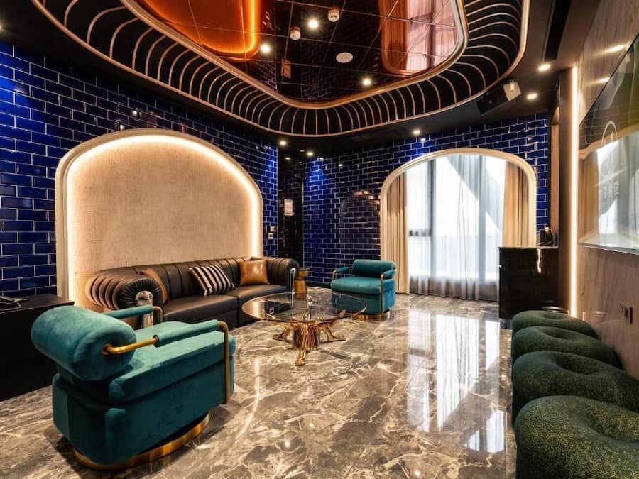 A modern lounge with a curved ceiling, a sofa, a coffee table, and a seating area with green upholstered chairs.