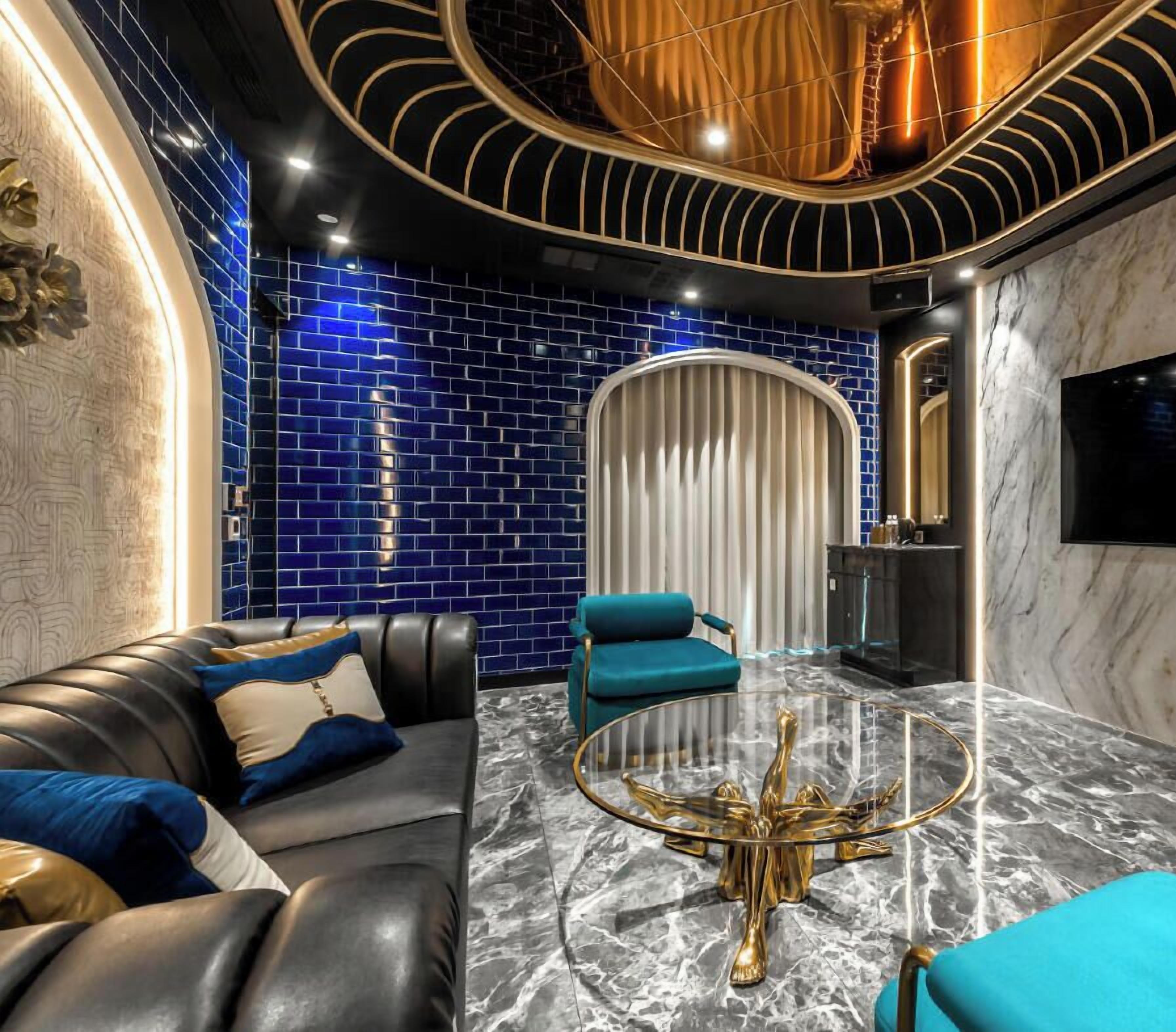 Una sala de estar moderna con un sofá de cuero, un sillón color turquesa y una mesa de centro de vidrio con patas doradas.