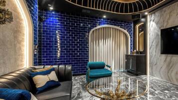 Una sala de estar moderna con un sofá de cuero, un sillón color turquesa y una mesa de centro de vidrio con patas doradas.