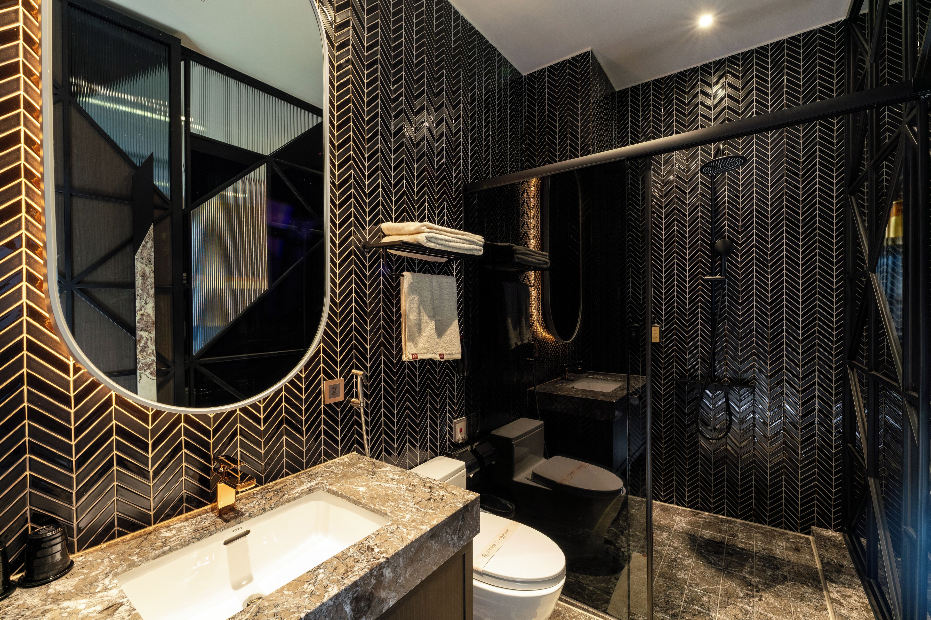 Uma casa de banho moderna com padrão de mosaico em losango preto e branco, um espelho grande, uma pia branca e um box de chuveiro de vidro.