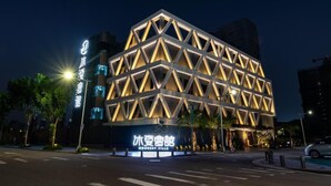 A modern building with a geometric facade, illuminated by internal lighting.