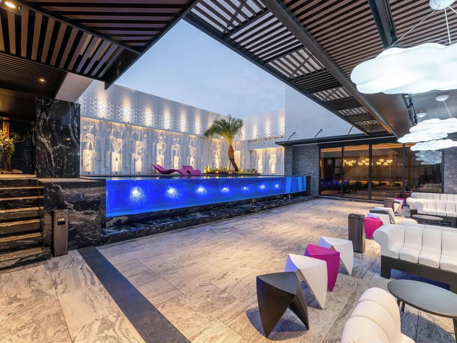 A modern indoor pool area with a blue-lit water feature, seating, and a patterned wall.