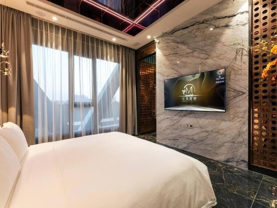 Habitación de hotel con una cama grande, un televisor de pantalla plana montado en una pared de mármol y vistas al exterior a través de amplios ventanales.