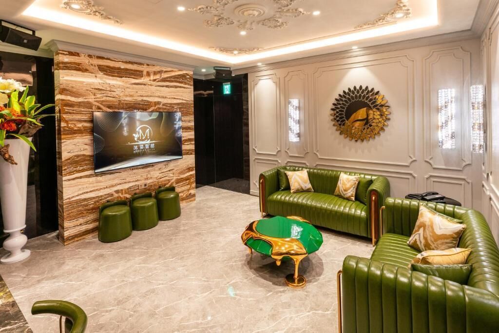 Vestíbulo con un televisor montado en una pared de mármol, sofás tapizados en verde, una mesa de centro verde y un elemento decorativo en la pared.