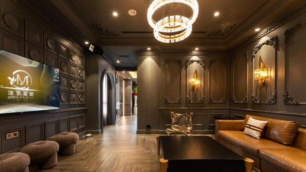 A luxurious interior with a dark wood floor, a black coffee table, a leather sofa, and a large TV screen displaying a logo.