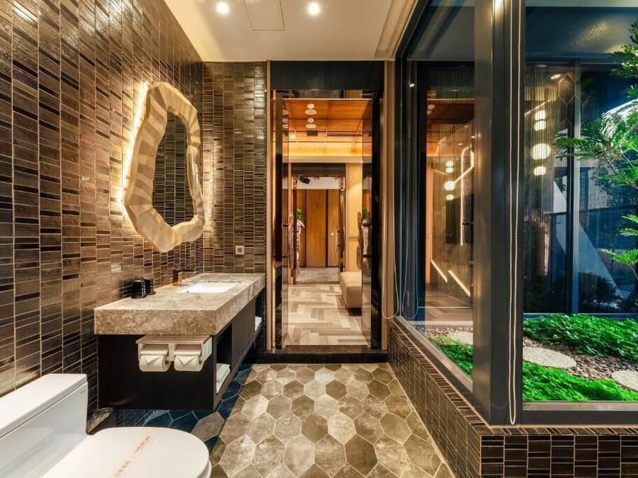 A modern bathroom with a large mirror, two sinks, and a glass enclosure with a view of greenery.