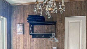 Una habitación con paneles de madera, un candelabro, un estante negro con ganchos y una puerta.