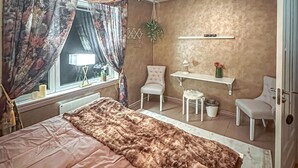 Un dormitorio con cama, escritorio, dos sillas, una mesita y una planta colgante.
