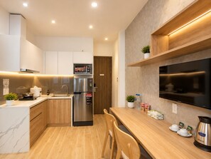 Una cocina moderna con microondas integrado, refrigerador de acero inoxidable, armarios de madera, una mesa de comedor de madera y un televisor de pantalla plana montado en la pared.