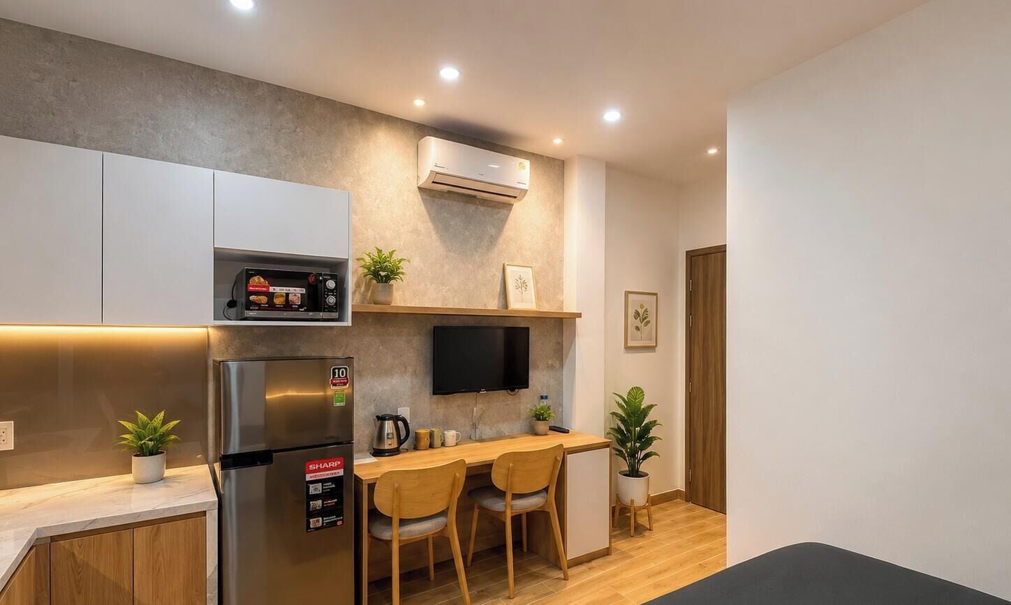 A modern kitchen with a built-in oven, a refrigerator, a flat-screen TV, and wooden chairs.