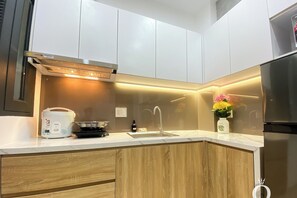 A modern kitchen with white cabinets, a stainless steel refrigerator, a built-in oven, and a countertop with a rice cooker and a vase with flowers. - Pandora House (Phuong Hoa Hung)