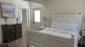 Une chambre à coucher avec un lit blanc, une commode, une chaise et un tableau accroché au mur.