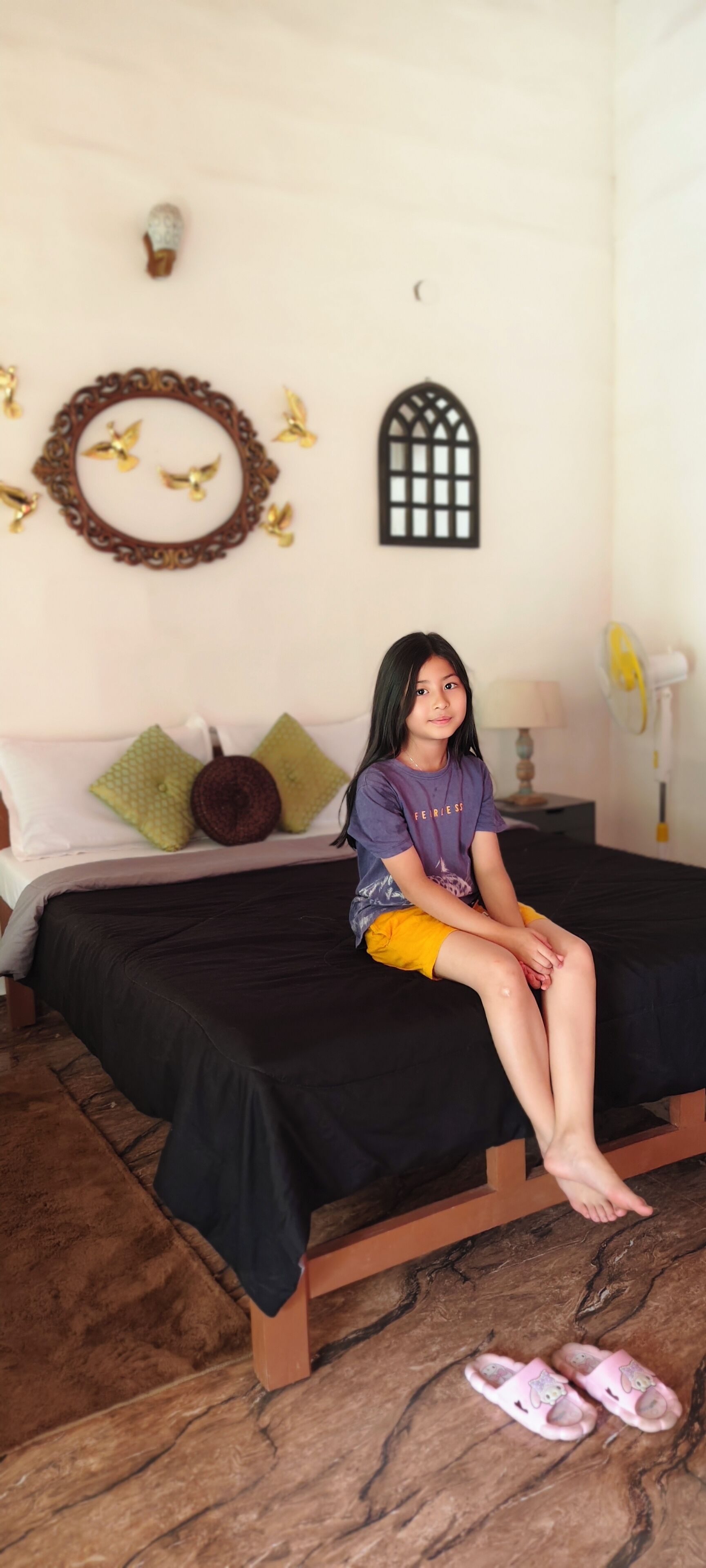Una habitación con cama, almohadas, un adorno en la pared y un ventilador.