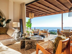 A spacious living area with a view of the sea, featuring a sofa, chairs, a coffee table, and a lamp. - Illume Mykonos | Villa with infinity pool sea view (Mykonos)