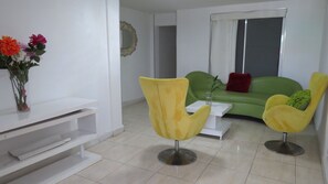 A modern living room with a green sofa, yellow chairs, a white coffee table, and a vase of flowers on a white console table.