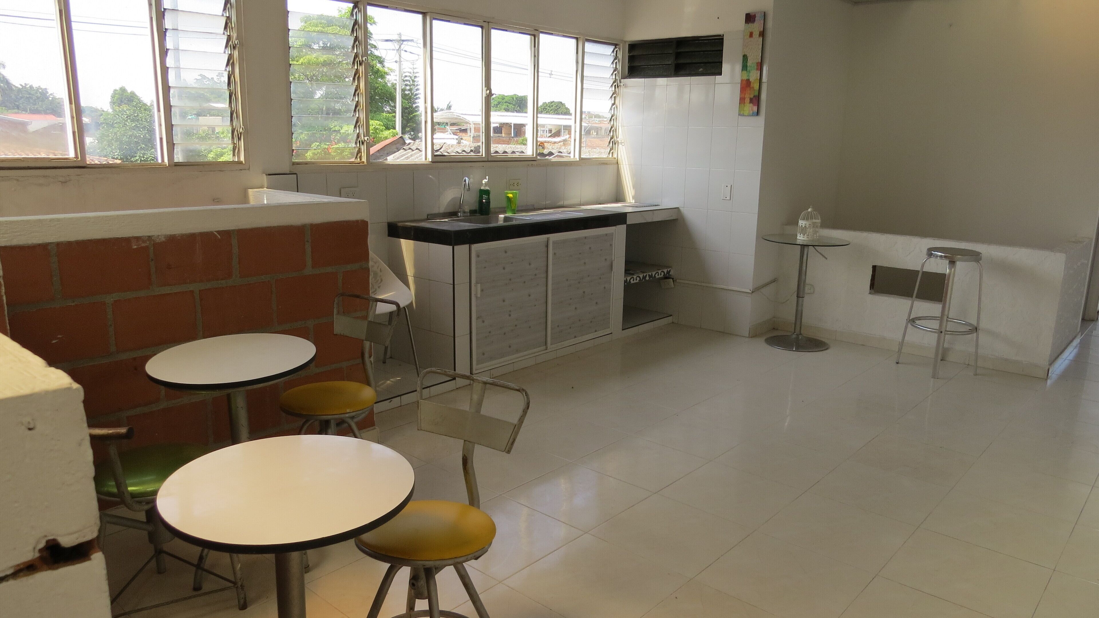 A kitchen with a sink, two stools, and a window with blinds.