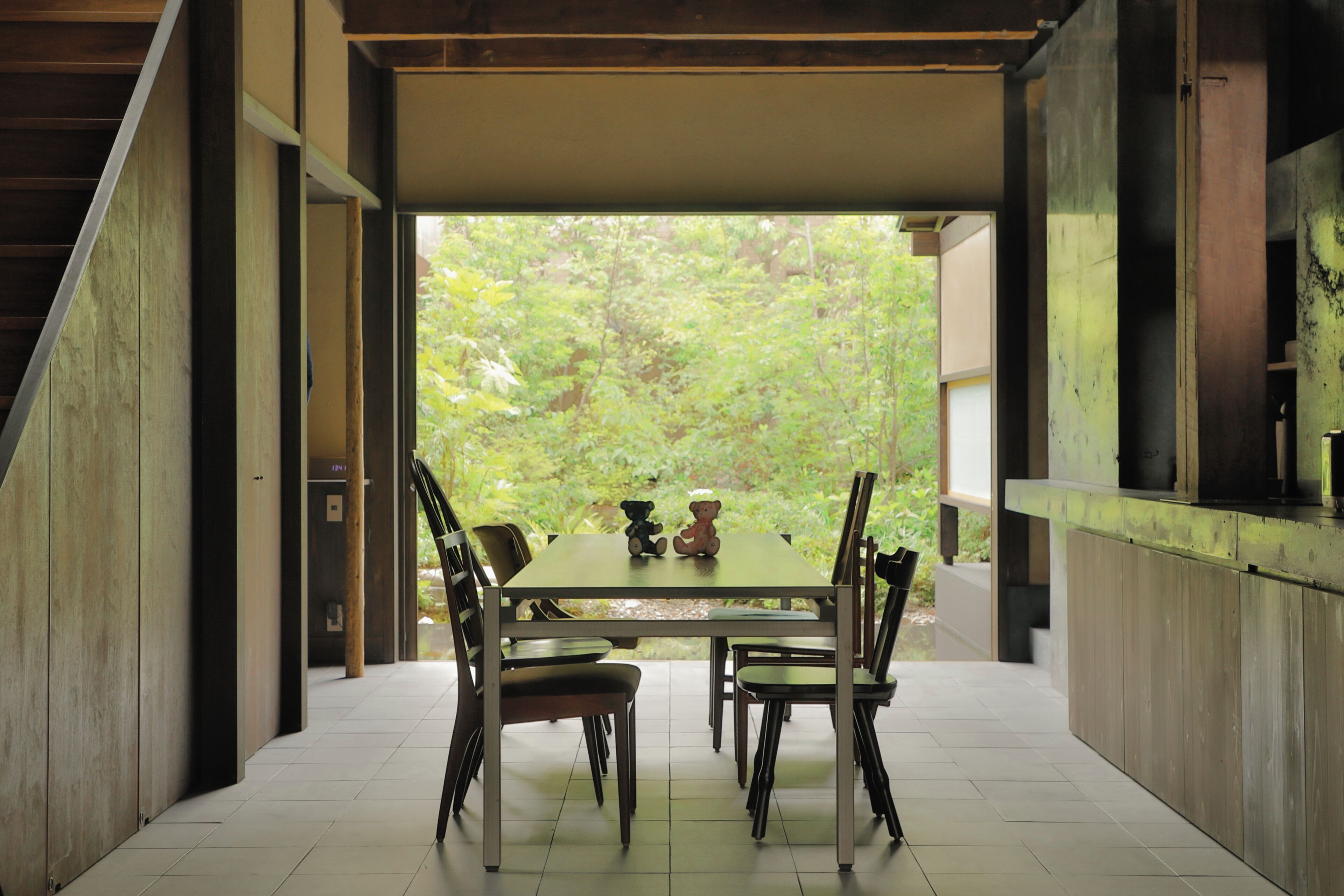 A dining area with a table and chairs, a view of greenery outside, and a modern architectural design.