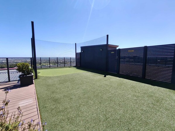 A rooftop terrace with artificial grass, a view of the city, and a black fence.