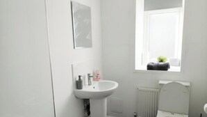 A bathroom with a white sink, a mirror, a window, and a radiator. - Carlisle 32 Esk Street Longtown (Longtown)
