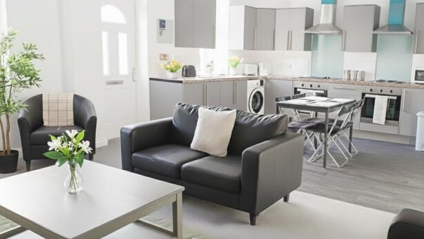 A modern living room with a sofa, coffee table, and a dining area with chairs. - Carlisle 32 Esk Street Longtown (Longtown)