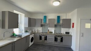 A modern kitchen with grey cabinets, a built-in oven, a microwave, and a washing machine. - Carlisle 32 Esk Street Longtown (Longtown)