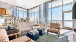 Ein geräumiger Balkon mit Sofa, Hocker und Sessel, einem gemusterten Teppich und Blick aufs Meer.