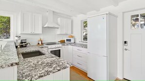 A modern kitchen with white cabinets, granite countertops, a stove, and a refrigerator.
