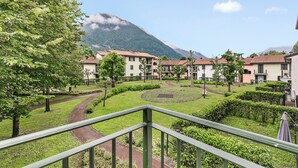 A residential area with a mountain in the background, a pathway, and a green lawn. - Porto Letizia Toscanini 4, Porlezza, Italy (Porlezza)