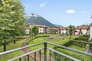 A residential area with a mountain in the background, a pathway, and a green lawn. - Porto Letizia Toscanini 4, Porlezza, Italy (Porlezza)