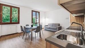 A modern kitchen with a stainless steel sink, a dining area with a table and chairs, and a grey sofa. - Porto Letizia Toscanini 4, Porlezza, Italy (Porlezza)