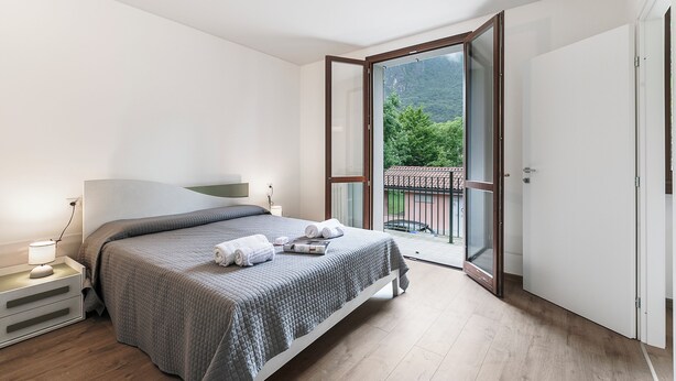 A bedroom with a bed, bedside table, and a view of a balcony. - Porto Letizia Toscanini 4, Porlezza, Italy (Porlezza)