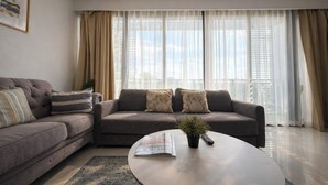 Ein modernes Wohnzimmer mit zwei Sofas, einem Couchtisch und einem großen Fenster mit durchsichtigen Vorhängen.
