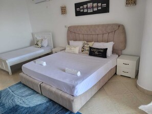 Een slaapkamer met een groot bed, een kleiner bed, twee nachtkastjes en een aan de wand bevestigd schilderij.