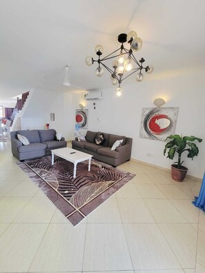 Een moderne woonkamer met een trap, een kroonluchter en een potplant.