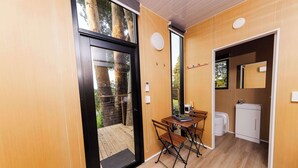 Una stanza con pavimento in legno, un tavolo con sedie, un piccolo lavandino e una porta che dà su un'area esterna.