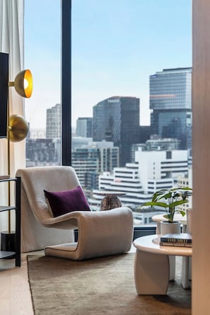 Ein modernes Wohnzimmer mit Blick auf die Stadt, ein bequemer Sessel, ein kleiner Tisch und ein Blumentopf.