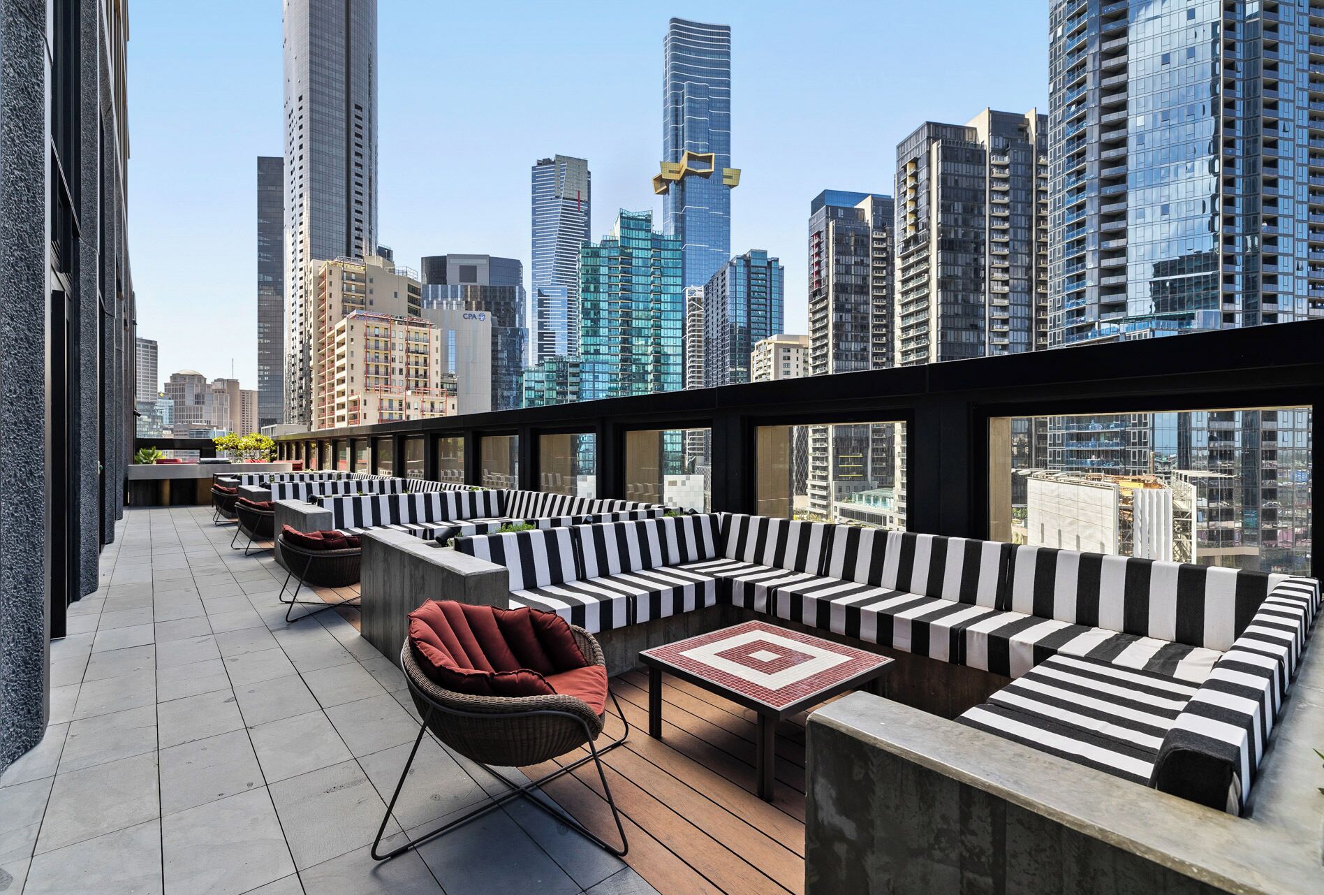 A rooftop terrace with black and white striped seating, a wicker chair, and a tiled table.
