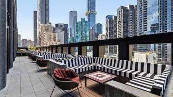 A rooftop terrace with black and white striped seating, a wicker chair, and a tiled table.