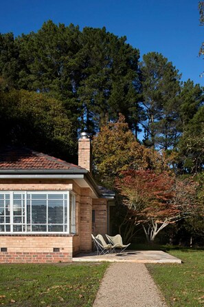 A house with a brick exterior, a chimney, and a paved driveway leading to two white chairs. - Polperro Farmhouse (Red Hill)