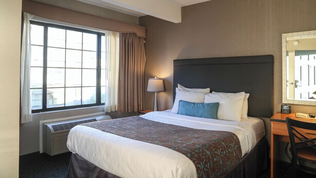A hotel room with a large bed, a desk, a chair, a window with curtains, a lamp, and a mirror. - Affordable SF Centrally Located Motel Room,Free Parking,Near Moscone,Breakfast (San Francisco)