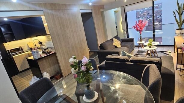 Un espacio moderno para vivir con una mesa de comedor de vidrio, un sofá y vistas de la ciudad a través de grandes ventanales.