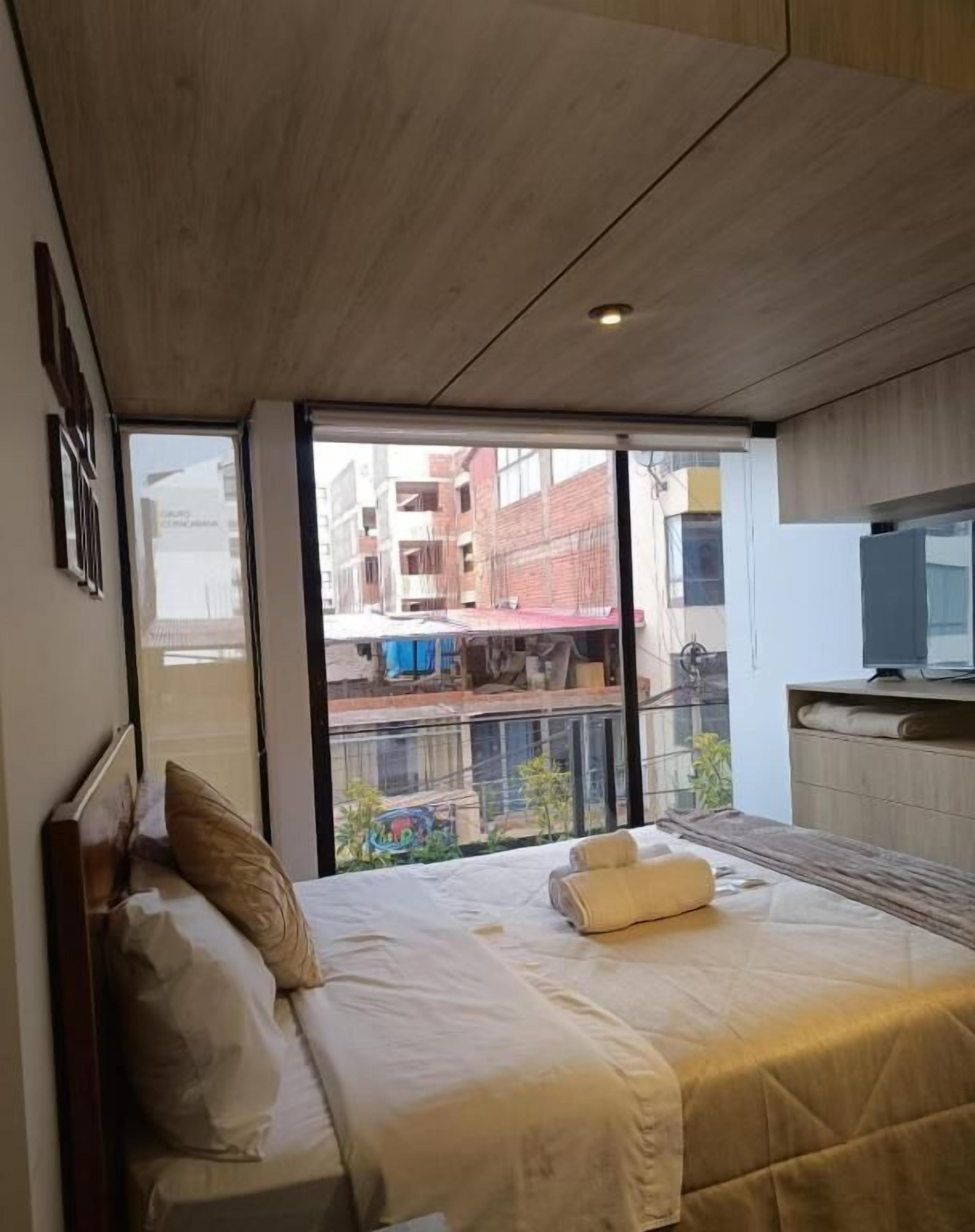 A bedroom with a bed, a TV, and a view of the outside.