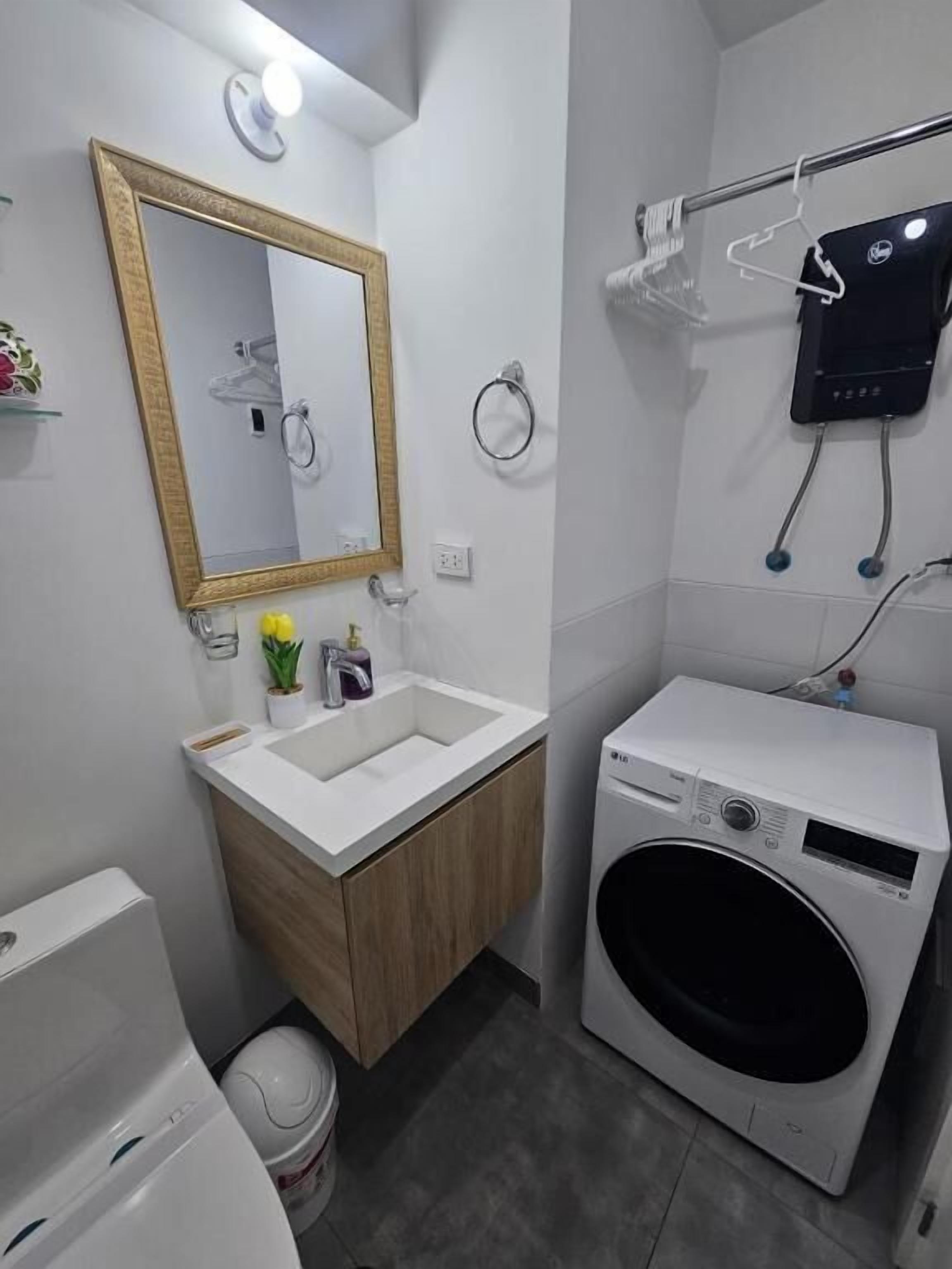 A compact bathroom with a sink, mirror, towel ring, and a washing machine.