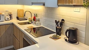 Una cocina moderna con armarios blancos, horno integrado, cafetera y una planta.